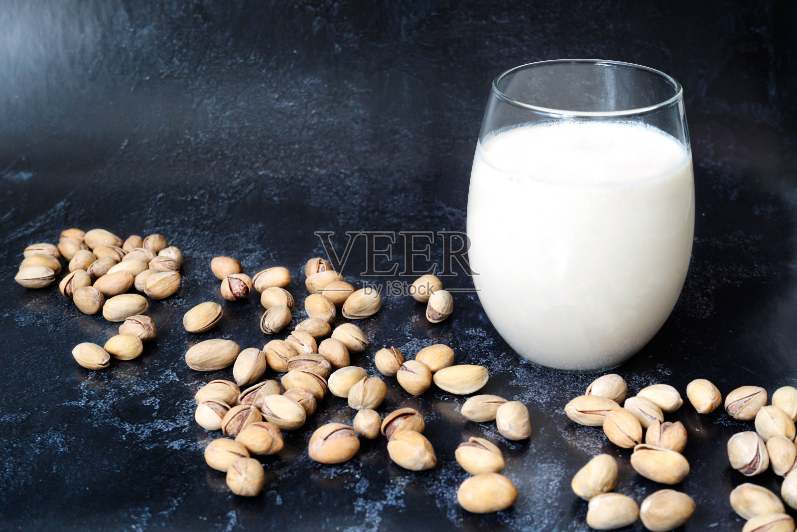 蔬菜开心果牛奶在一个玻璃站在黑暗的背景。附近散落着带壳的开心果。素食食品，健康有机食品，减肥食品。富含蛋白质和维生素的食物照片摄影图片