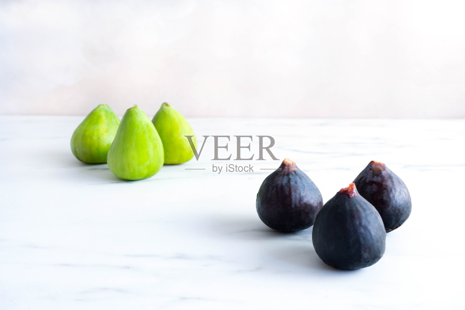 三棵紫色和三棵绿色的无花果树，靠着一堵浅色的墙，躺在一张白色的桌子上。美味的成熟芳香的无花果是自制果酱或蜜饯的好原料。金秋丰收，金秋硕果累累照片摄影图片