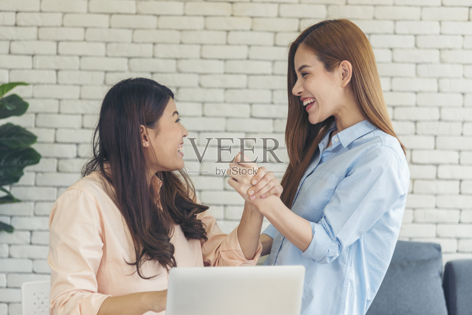 亚洲同事友谊在工作中面带微笑。幸福的两个女同事一起工作，在办公室的办公桌上开会。与笔记本电脑创业公司合作的团队合作伙伴照片摄影图片