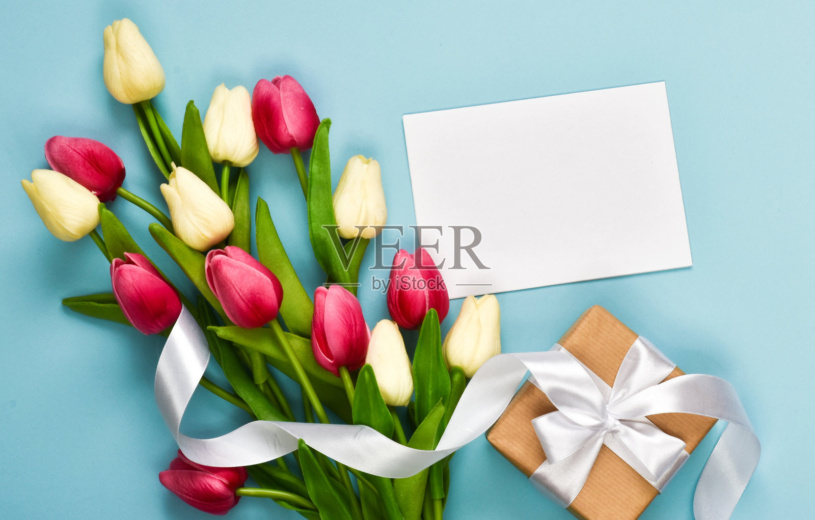 一束郁金香，一个礼盒和浅蓝色背景的纸卡照片摄影图片