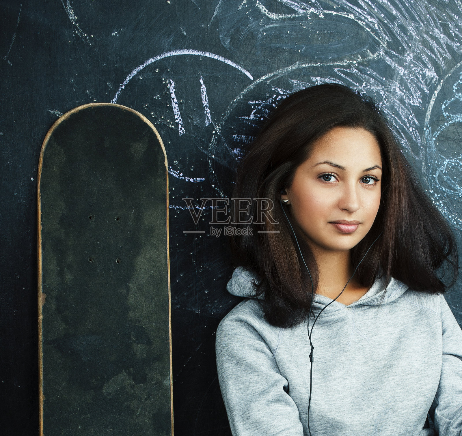 年轻可爱的十几岁女孩在教室的黑板上坐在桌子上微笑，现代潮人的概念照片摄影图片