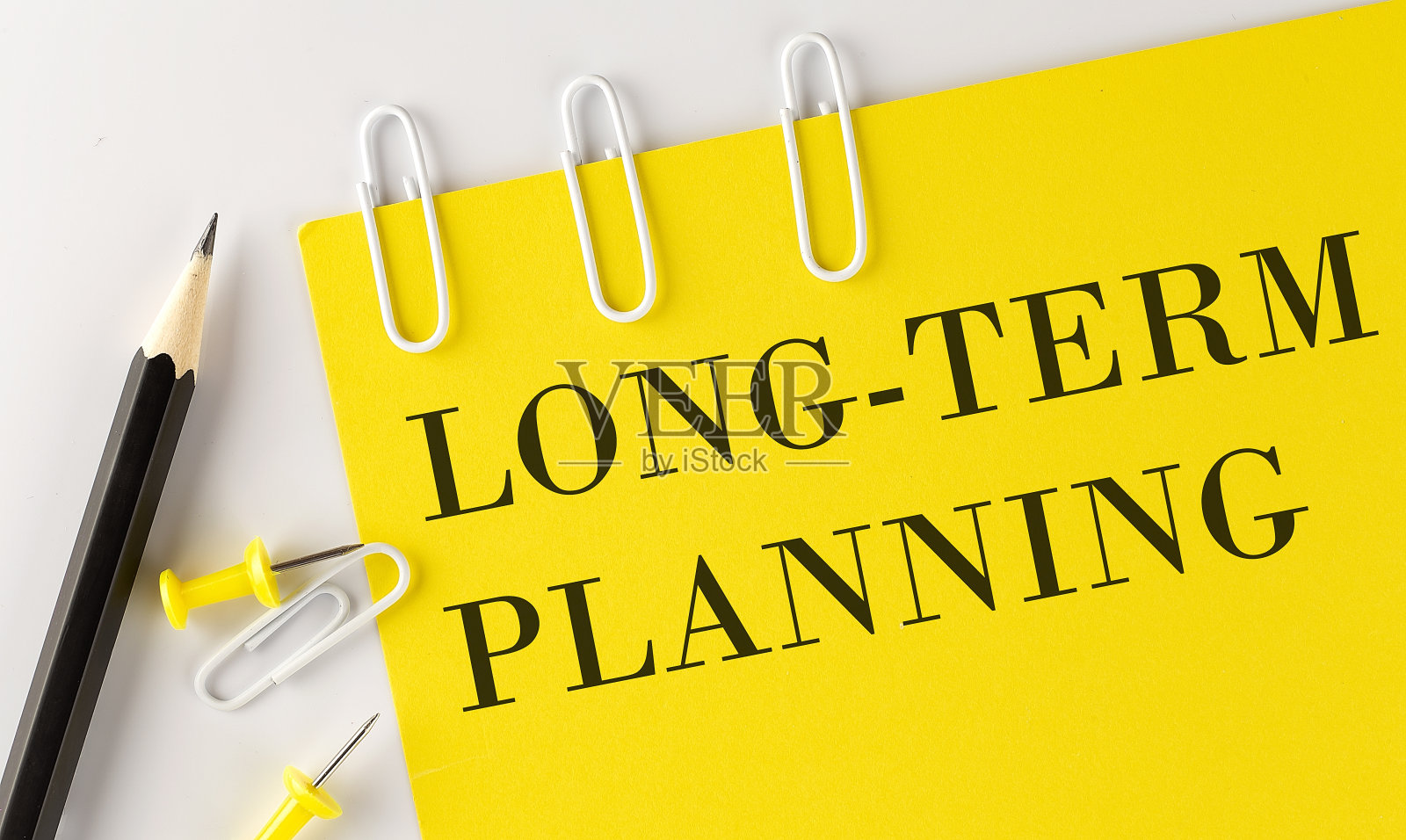 长期规划字在黄色纸张上，办公工具在白色背景上照片摄影图片