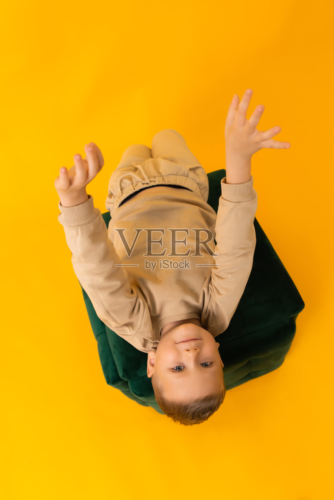 在一间画室里，黄色背景的小男孩躺在绿色的垫子上打招呼照片摄影图片
