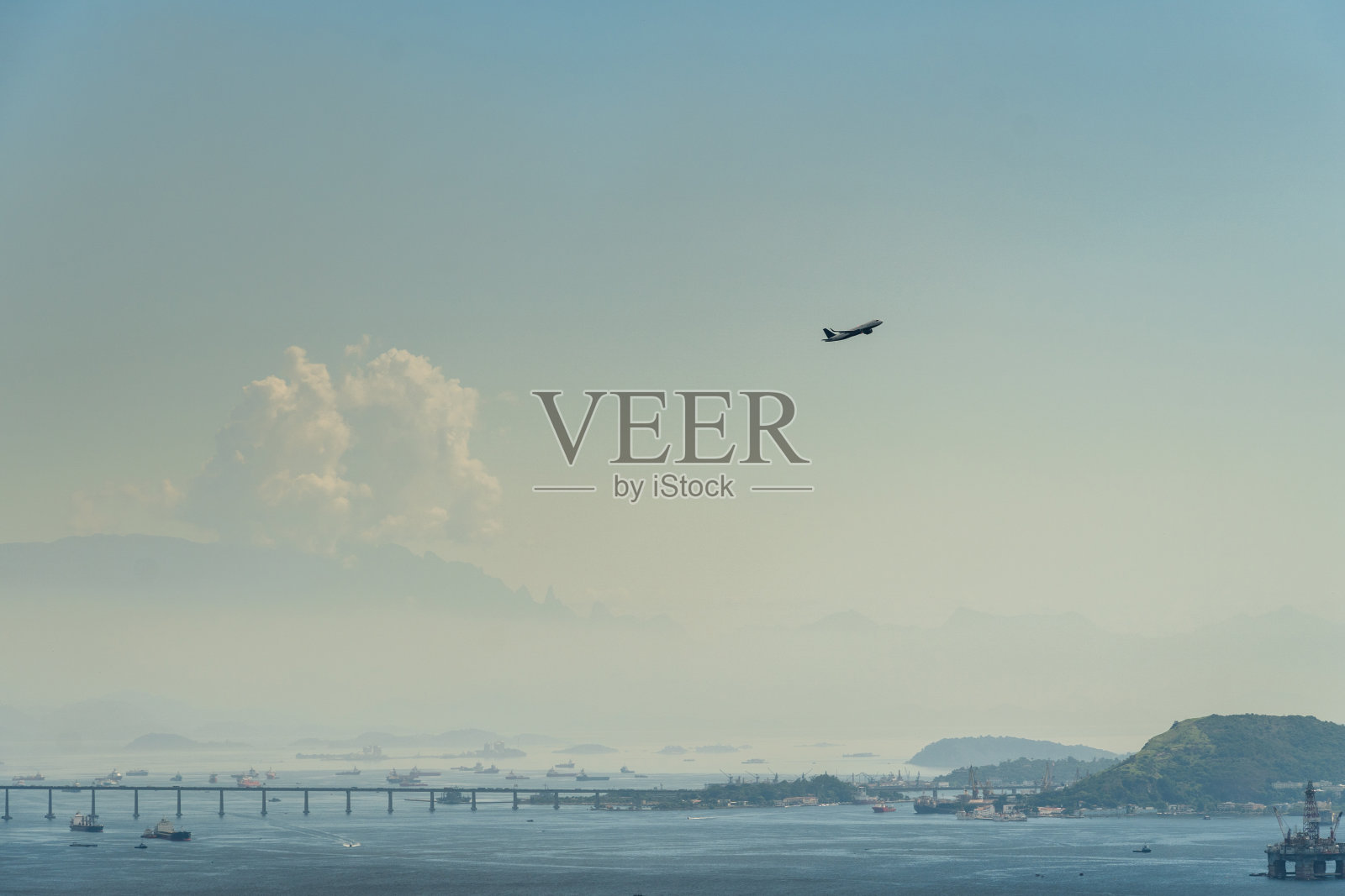 一架飞机从巴西里约热内卢的机场跑道上起飞。里约热内卢Niterói背景中的桥、山和船。黎明时分有一点雾照片摄影图片