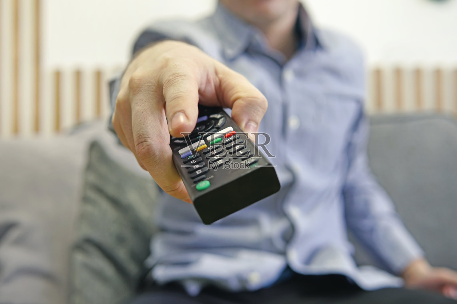 手里拿着遥控器的人在看体育频道时按下了遥控器上的按钮。遥控器在手中特写。切换频道。照片摄影图片