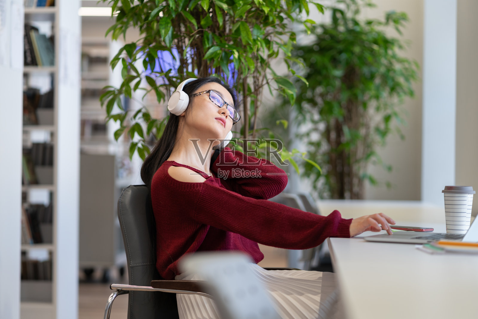 劳累过度的女学生摸痛了脖子，筋疲力尽的工作在图书馆准备毕业考试照片摄影图片