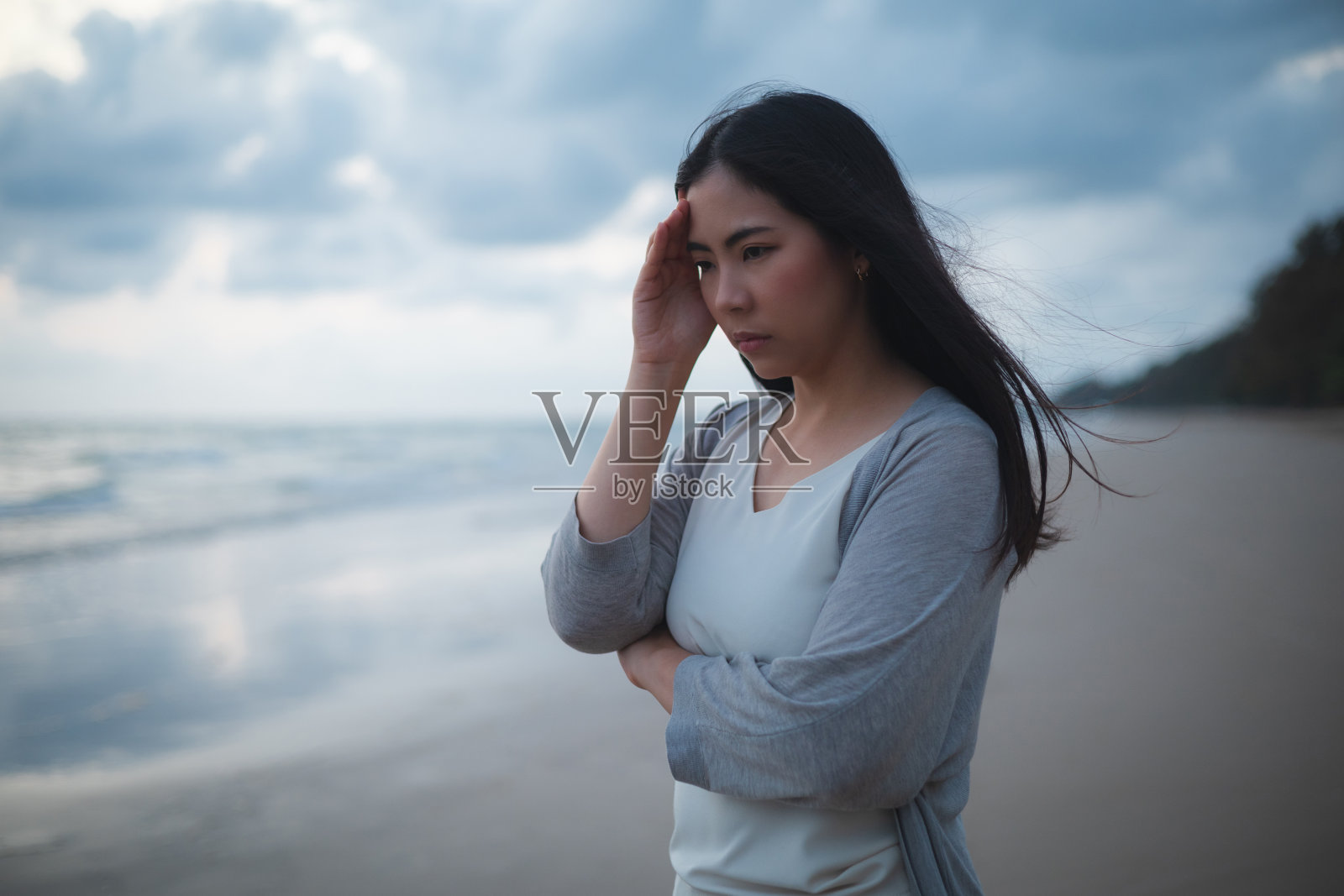 傍晚，一个悲伤而紧张的亚洲女人独自站在沙滩上。戏剧性的氛围。生活中失望。她独自站在那里哭照片摄影图片