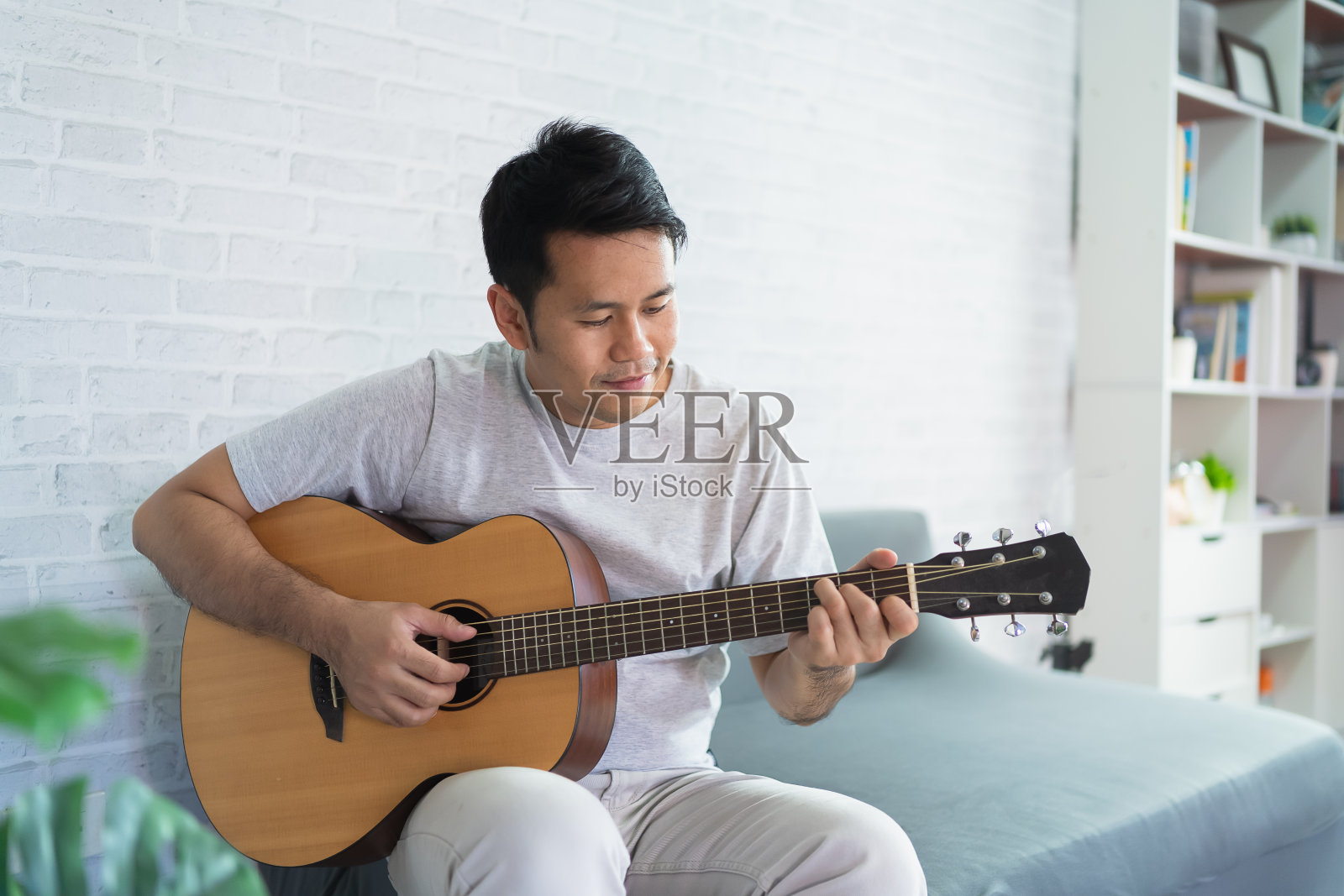 亚洲人弹吉他，而坐在沙发在灯光客厅。亚洲人在家里弹吉他时写歌。作曲作曲概念。照片摄影图片