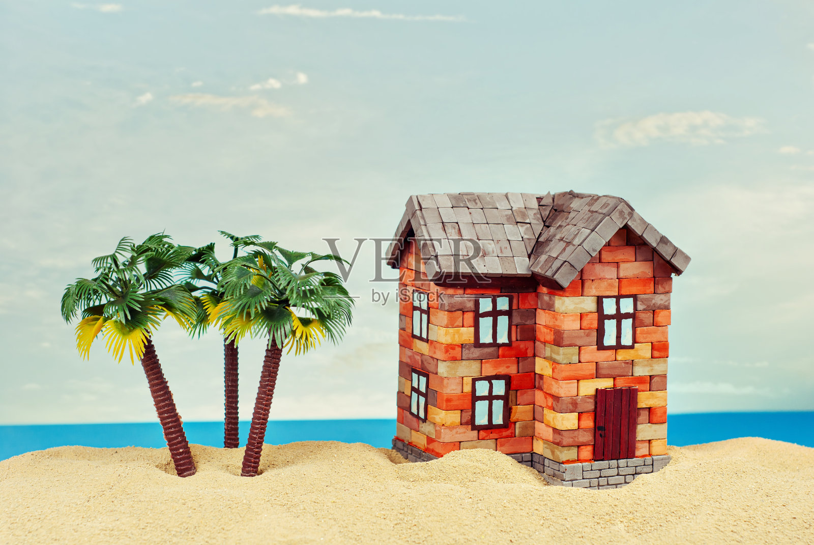 在沙滩上模拟一座房子。以大海和蓝天为背景的海滨别墅。买房和抵押贷款的概念。房子附近有棕榈树和天堂岛。照片摄影图片