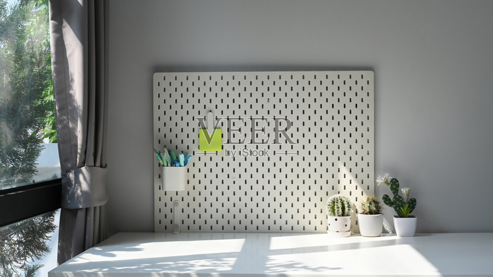 在家庭办公室的浅色墙壁上挂着钉板，上面有笔筒和便条。照片摄影图片