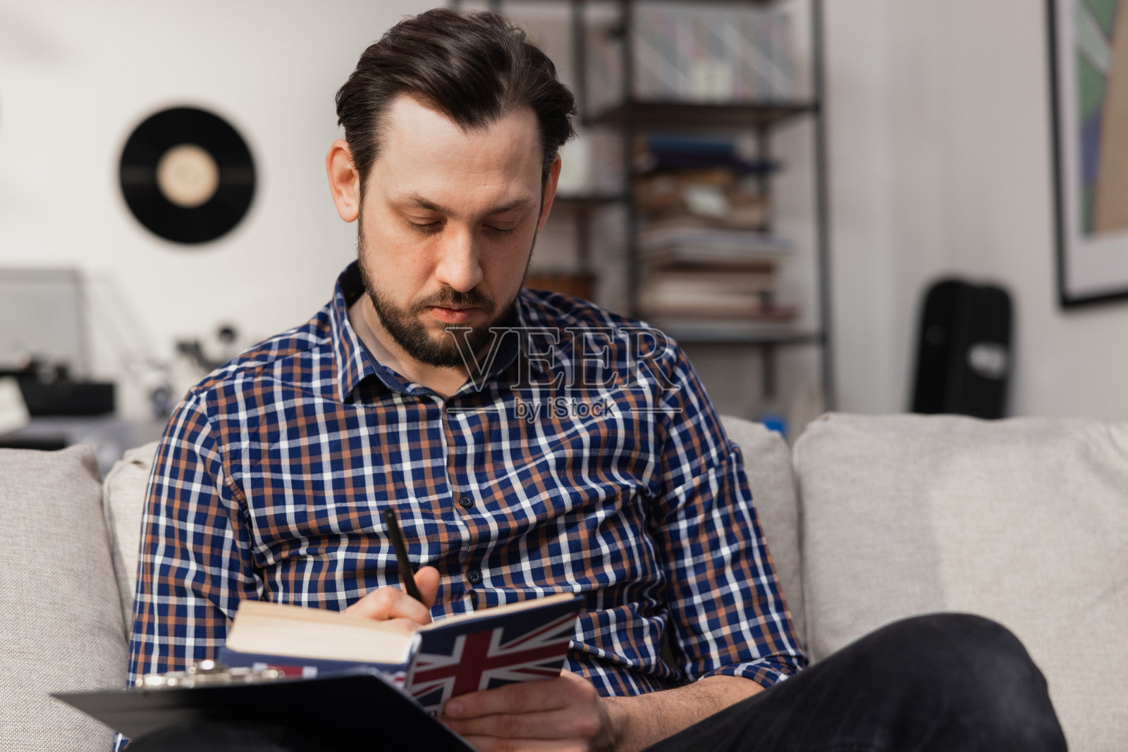 一个英俊的男人坐在家里客厅的沙发上读英语词典。一个穿着牛仔衬衫的中年男孩为大学考试做准备照片摄影图片