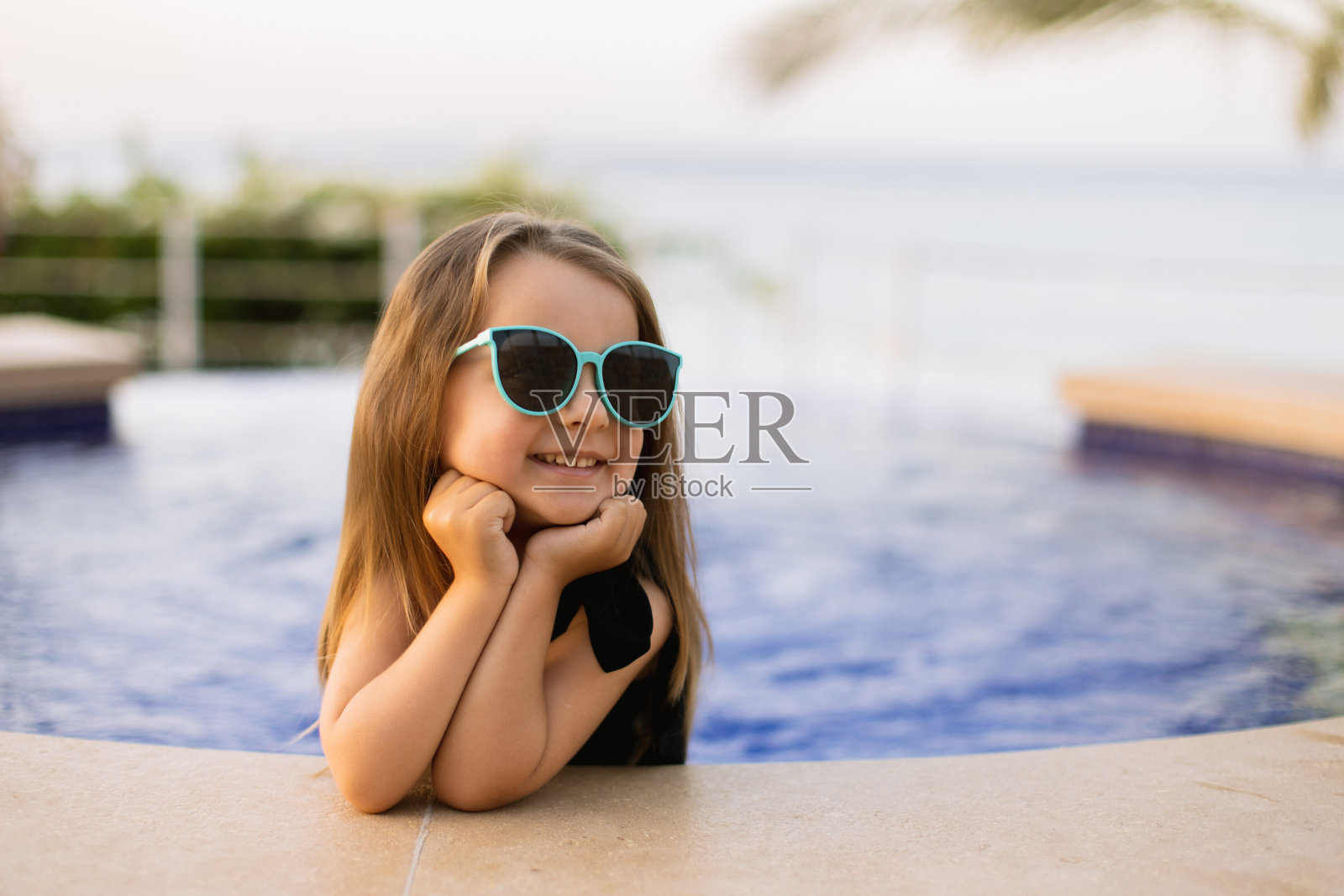 白人小女孩的肖像把她的手放在池边和她的脚在水里。照片摄影图片