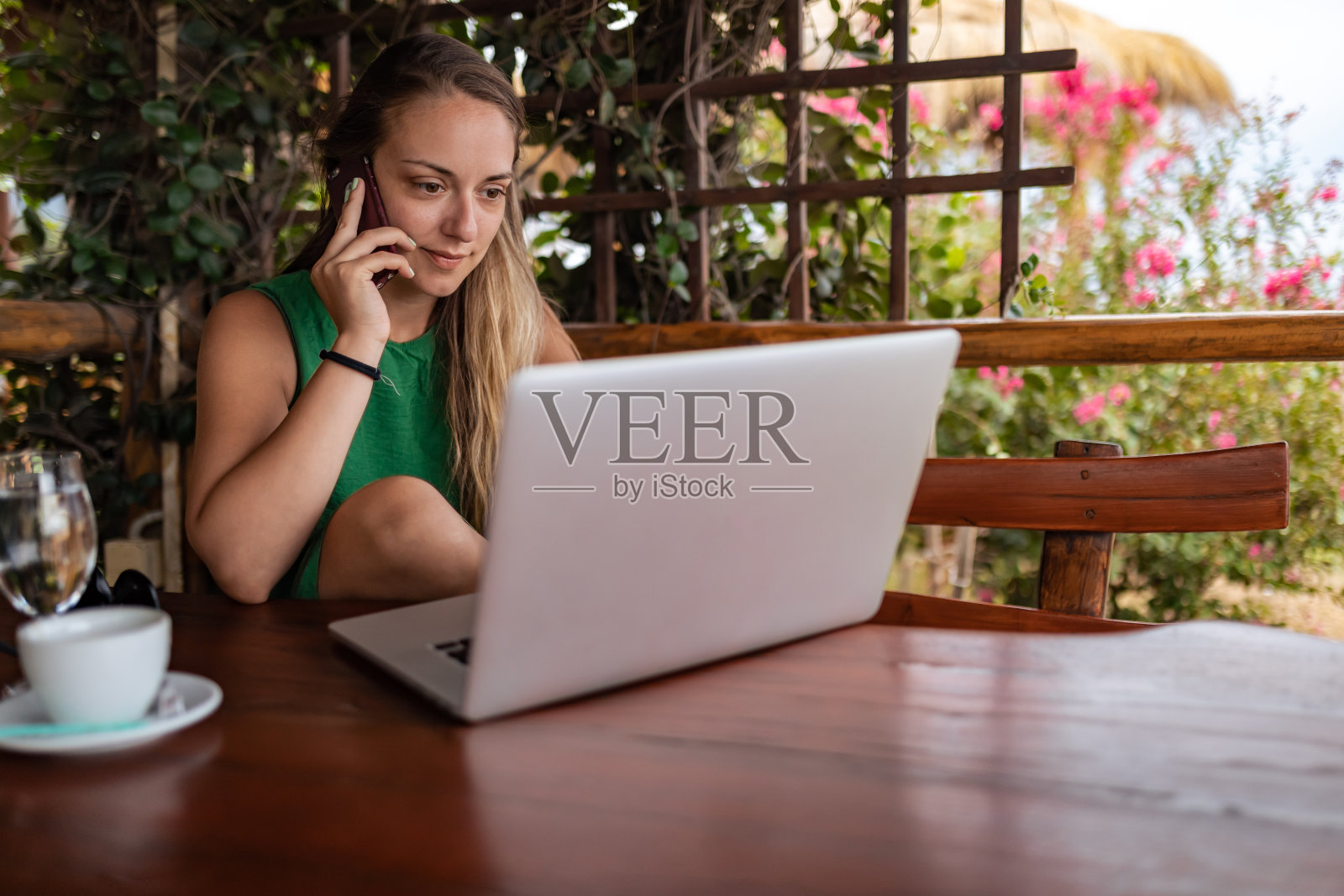 一位女商人坐在木凳上，一边打电话，一边用笔记本电脑。照片摄影图片