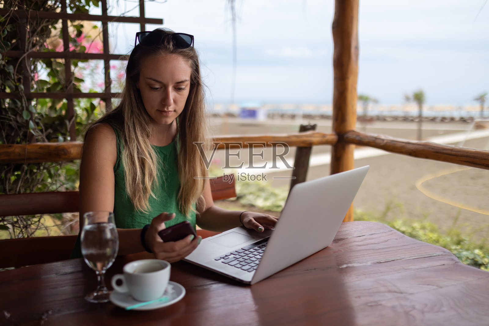 一名年轻女子坐在海滩上的一家咖啡店里，拿着手机与同事打商务电话。照片摄影图片