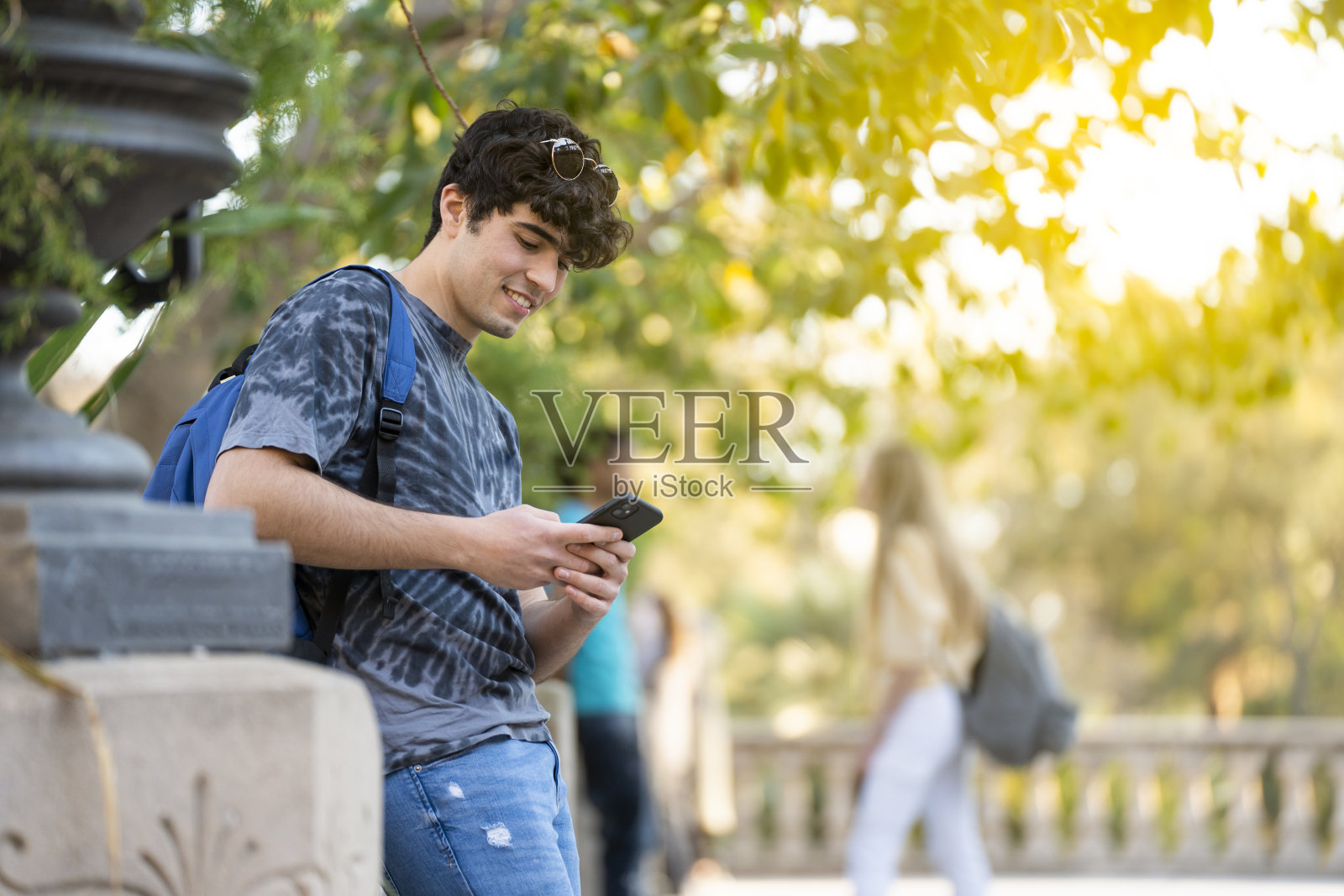 一个年轻的男学生在街上看着他的手机微笑照片摄影图片