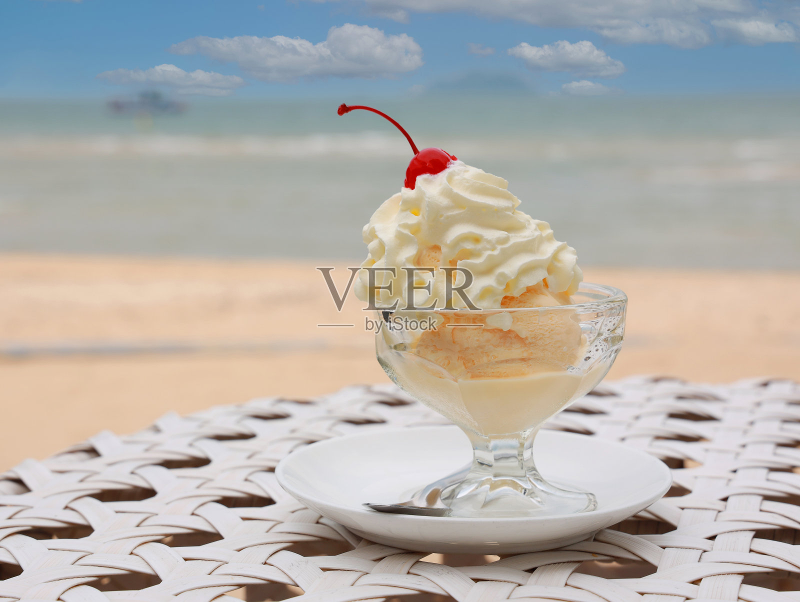 沙滩附近的桌子上放着一碗美味的香草冰淇淋，上面印着夏日度假的图案照片摄影图片