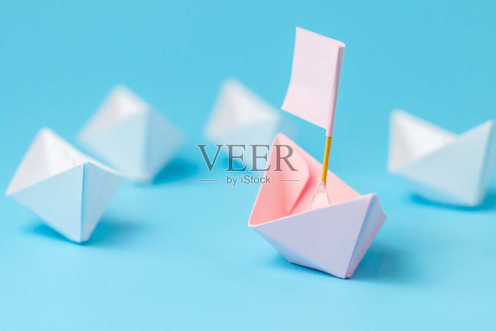 领导的概念。在白色纸船中间，带旗的粉红色纸船。一个领导领导其他船只。照片摄影图片