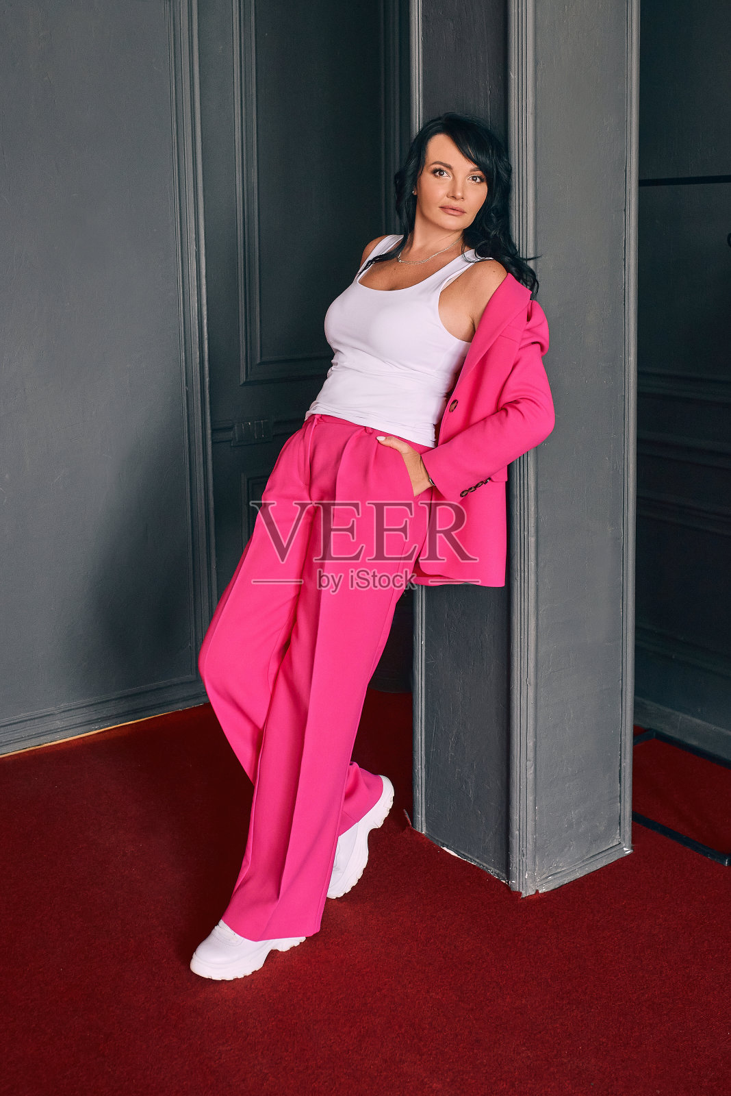 美丽的时尚女演员在红色天鹅绒窗帘的背景粉红色的西装。剧场、风格、时尚、事件概念照片摄影图片