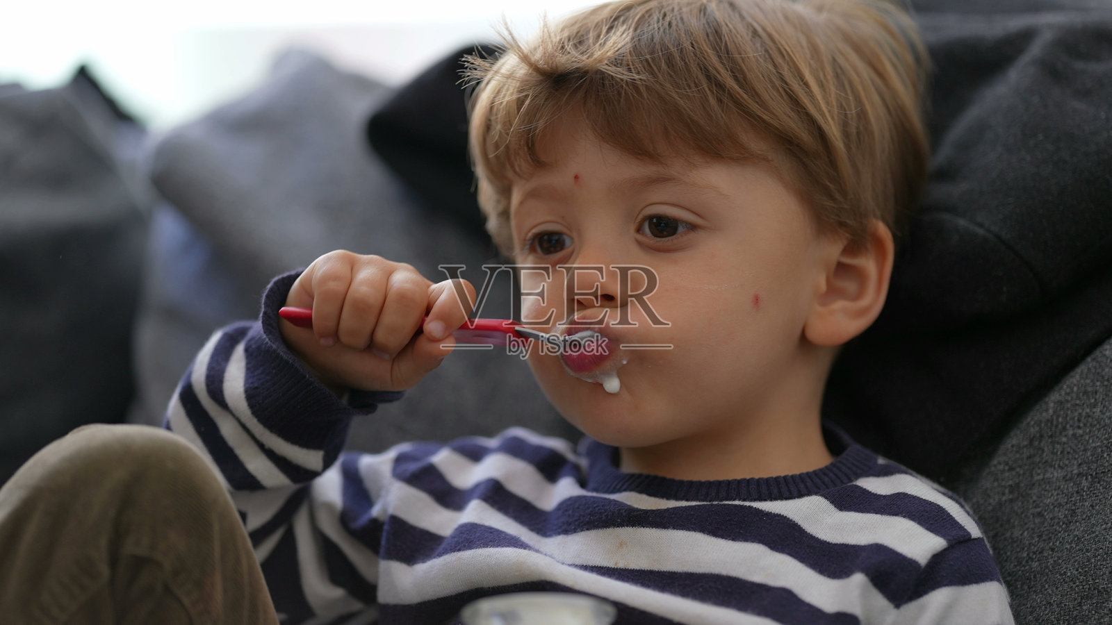 一个小男孩坐在沙发上用勺子吃酸奶照片摄影图片