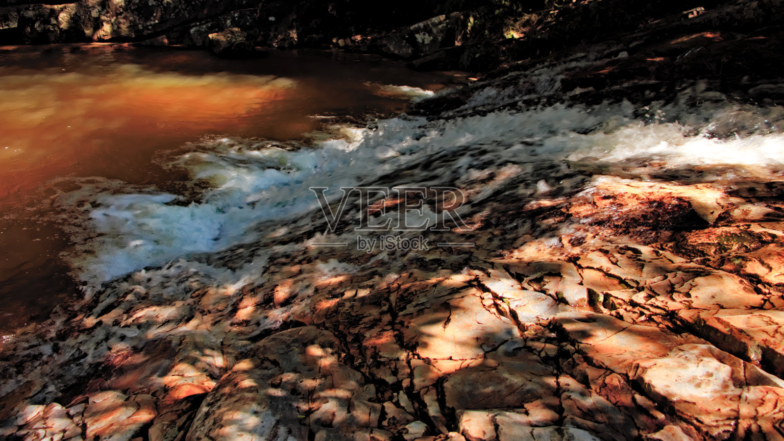 溪水流过岩石，点缀着光和影，流进一个小湖里。照片摄影图片