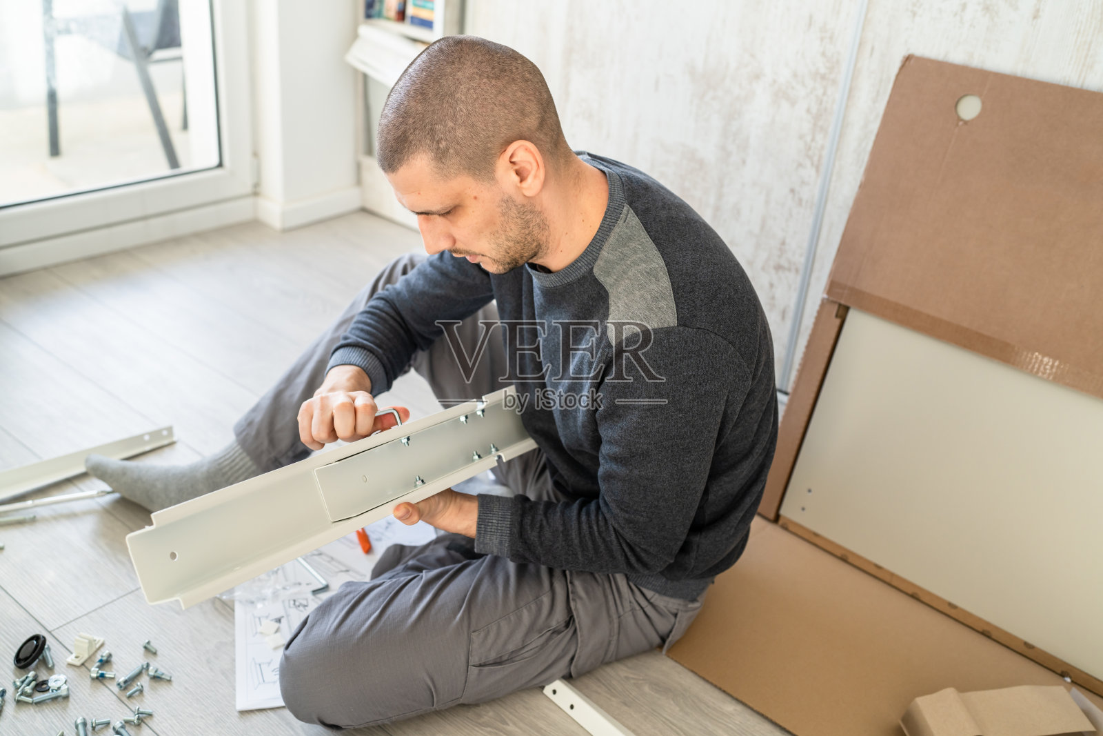一个男人，白人男性，坐在家里的地板上组装，自己组装家具，自己组装，拿着零件和说明书，真人复制空间照片摄影图片