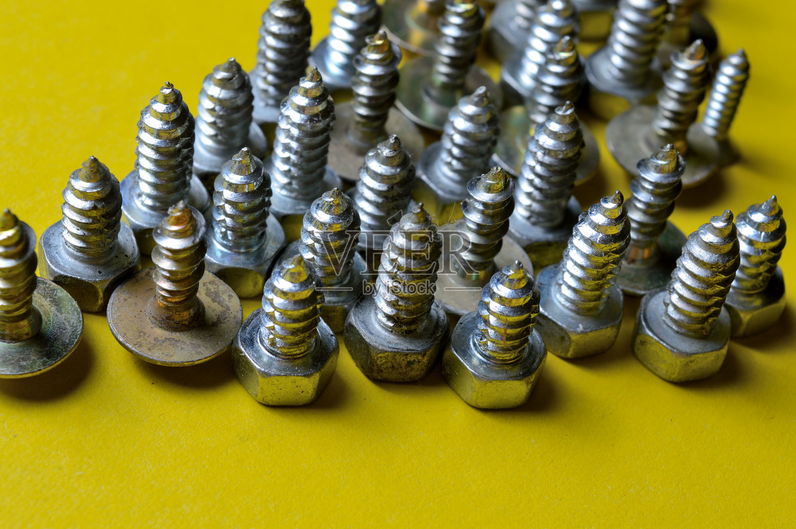 不同尺寸的螺母螺栓和自攻螺钉放在黄色背景上。特写镜头照片摄影图片