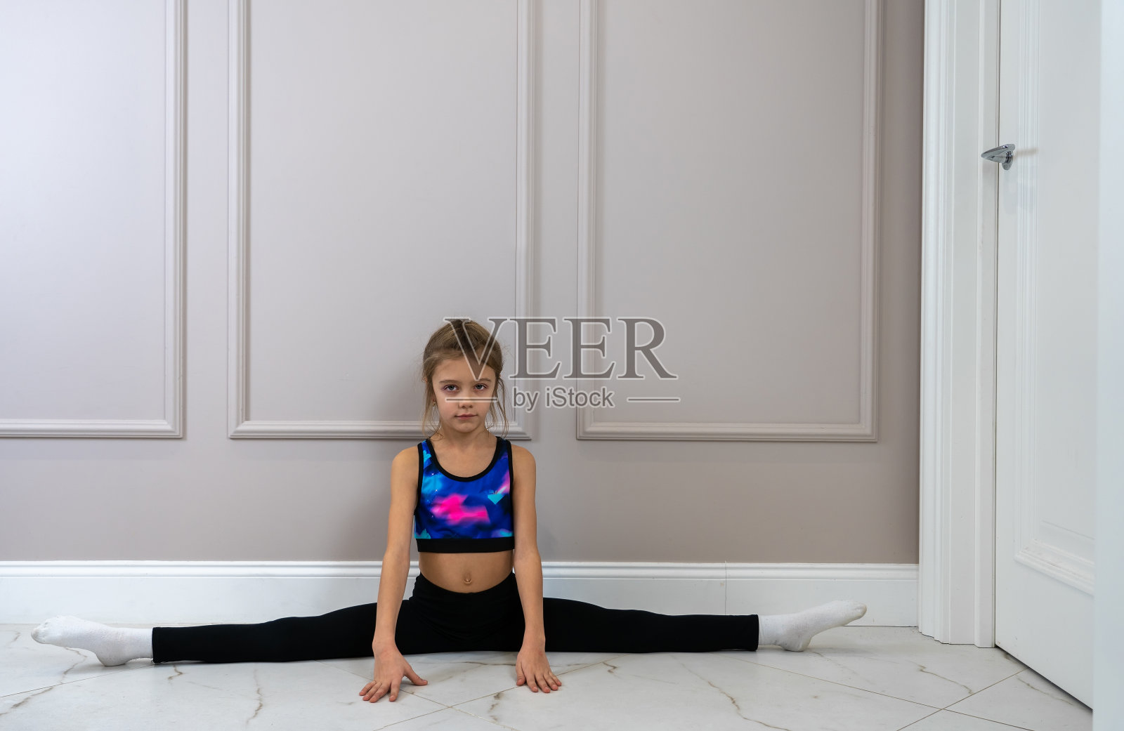 穿着运动服的小女孩在客厅的地板上做劈叉照片摄影图片