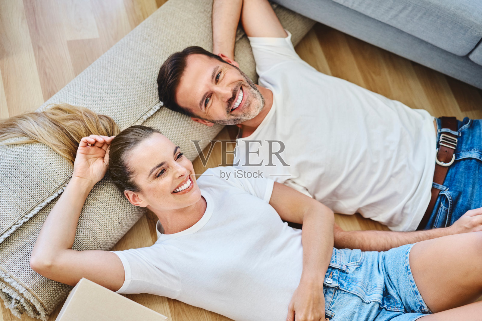 躺在新家地板上笑的夫妻。无忧无虑的人们搬进来了。照片摄影图片