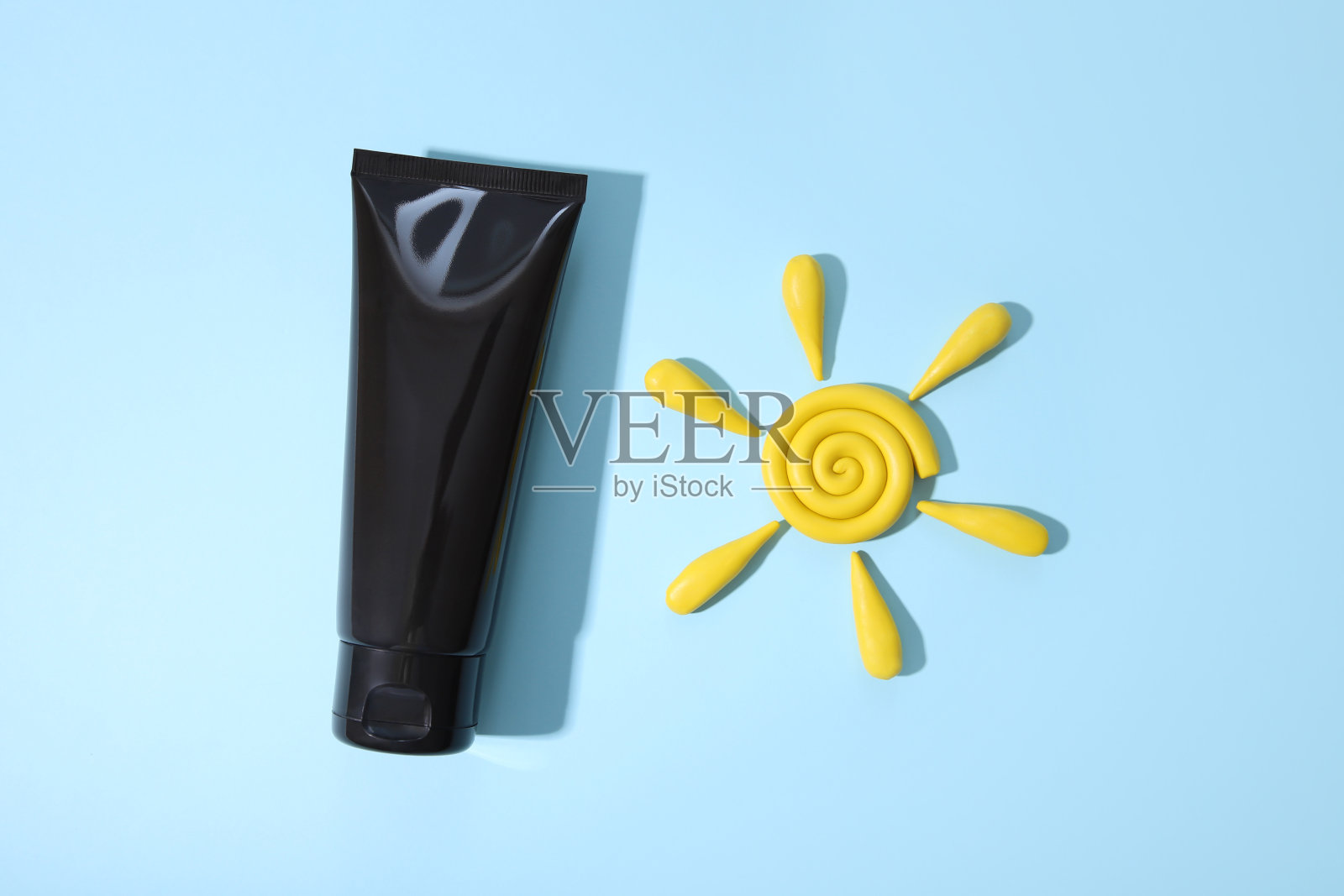 黑色挤压瓶化妆品管和黄色橡皮泥造型粘土太阳在蓝色背景与阴影。日常乳霜，啫喱，护肤，防晒，保湿。化妆品空瓶容器。照片摄影图片