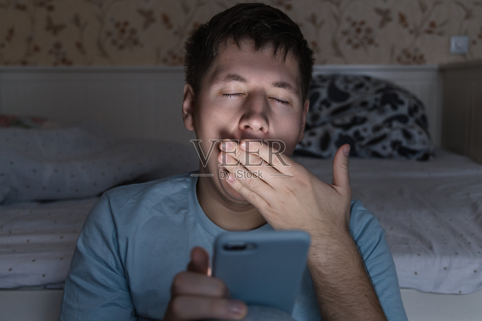 困倦的男子打着哈欠，用手捂住嘴。男人半夜醒来，在网上冲浪，不能入睡。照片摄影图片