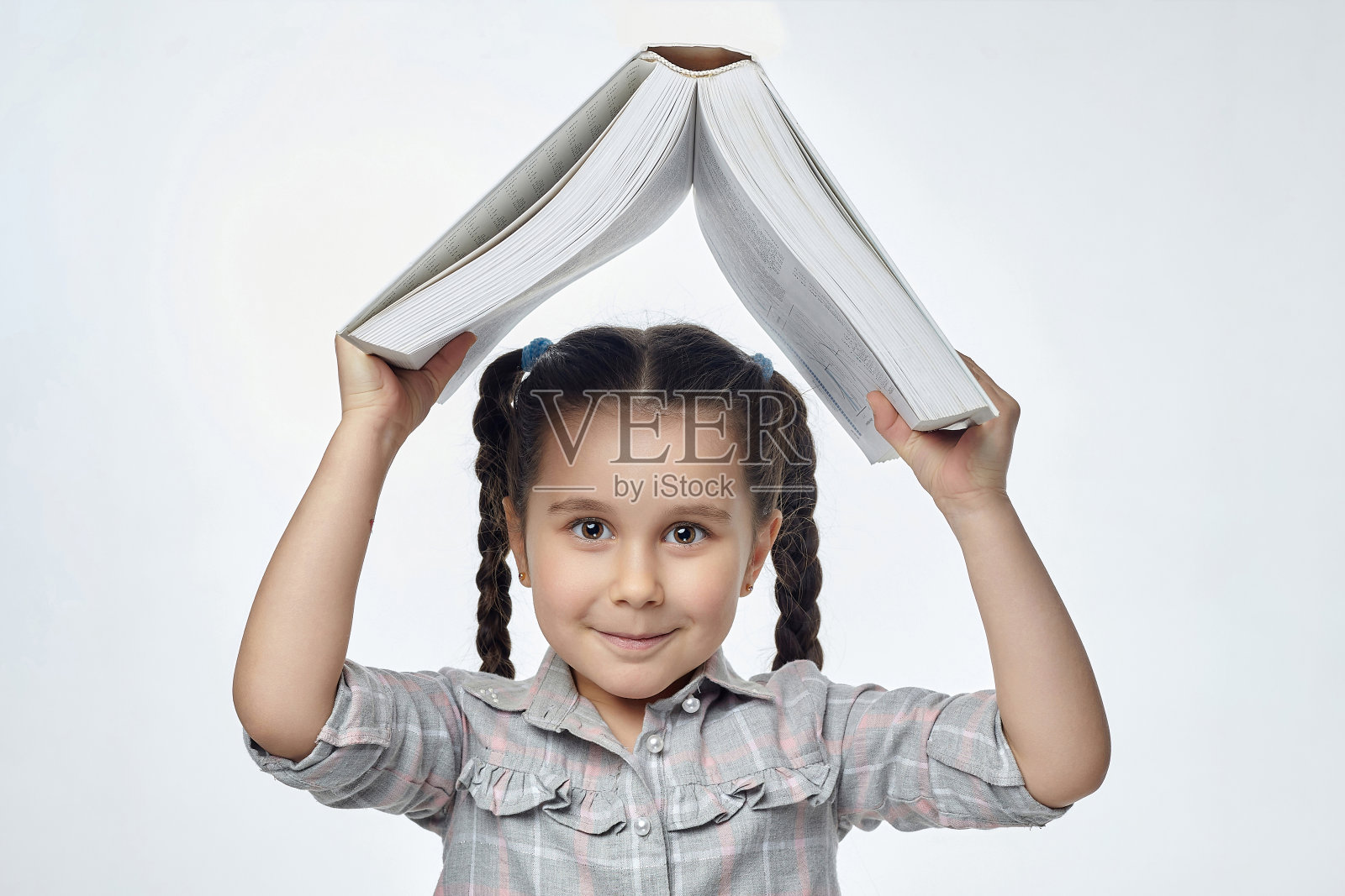 扎着辫子的小女孩面带微笑，把一本大书举过头顶照片摄影图片