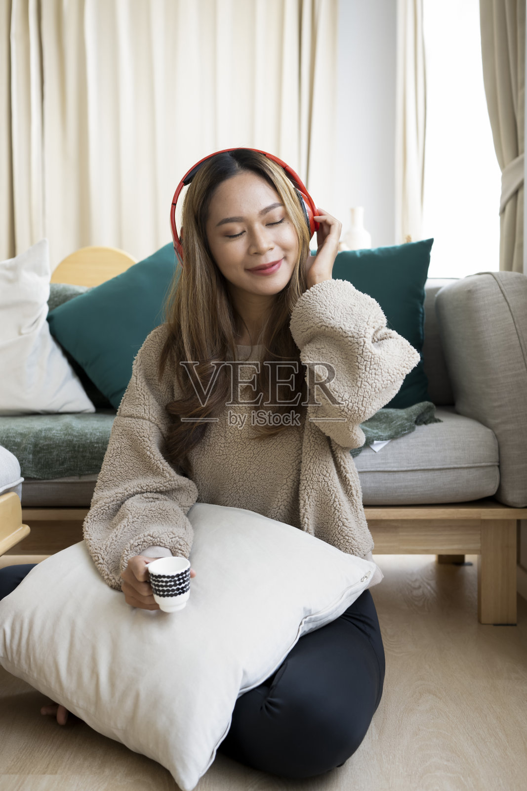 轻松的亚洲女人听音乐与耳机和喝咖啡在客厅。照片摄影图片