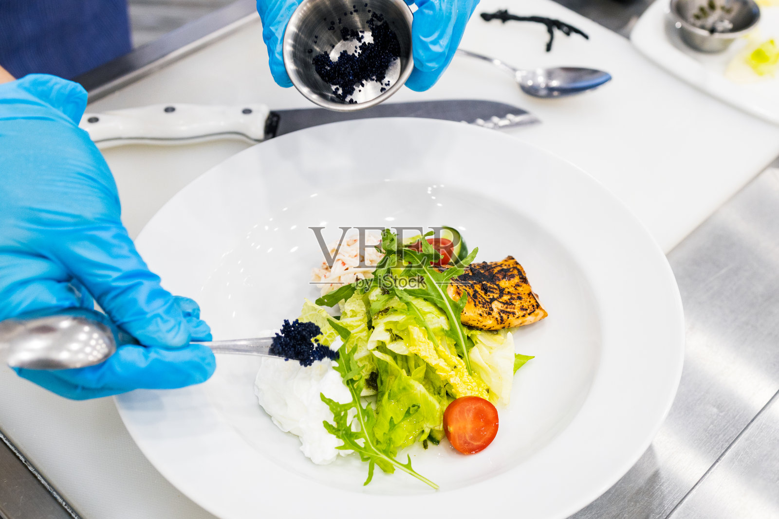 将勺尖上的黑鱼子酱加到白色盘子里的沙拉中照片摄影图片