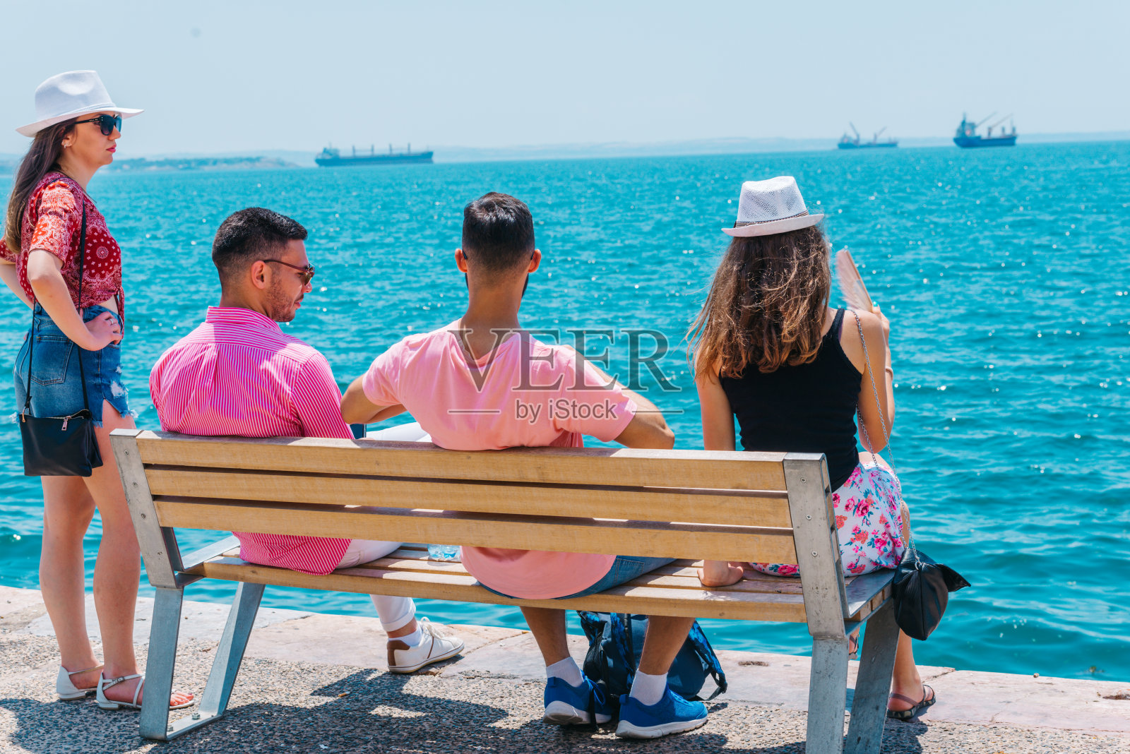 两对游客夫妇坐在长椅上，欣赏着壮丽的海景。照片摄影图片