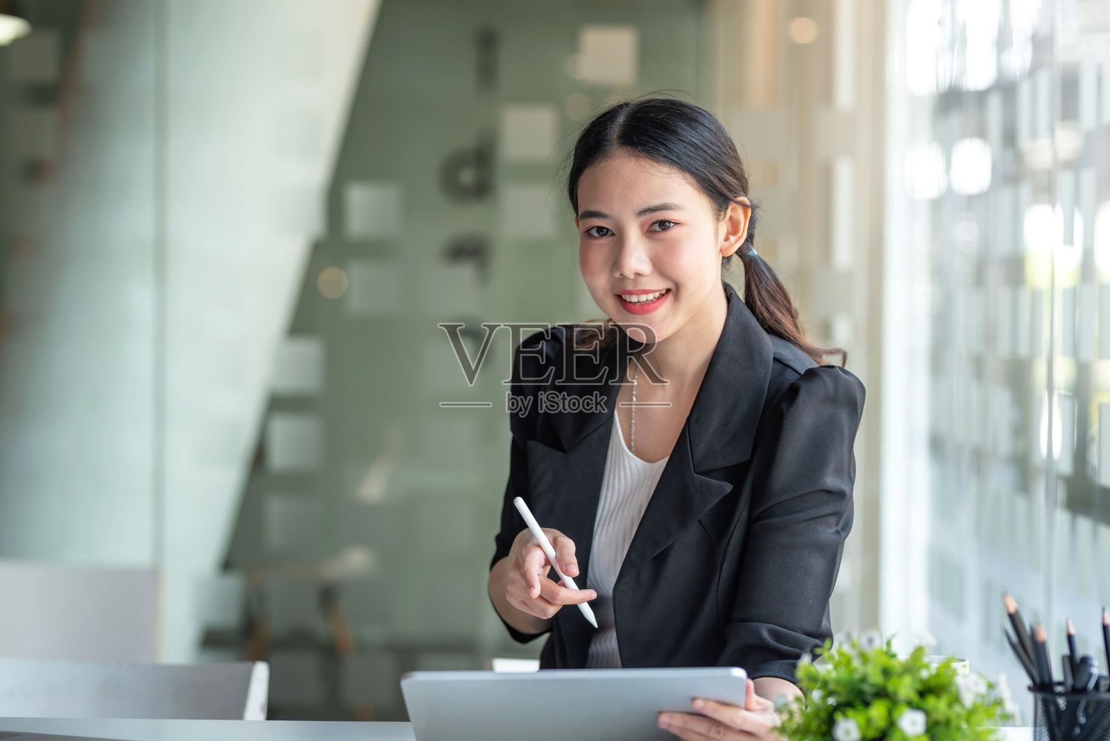 美丽年轻的亚洲女商人微笑着坐在办公室的平板电脑上工作。照片摄影图片