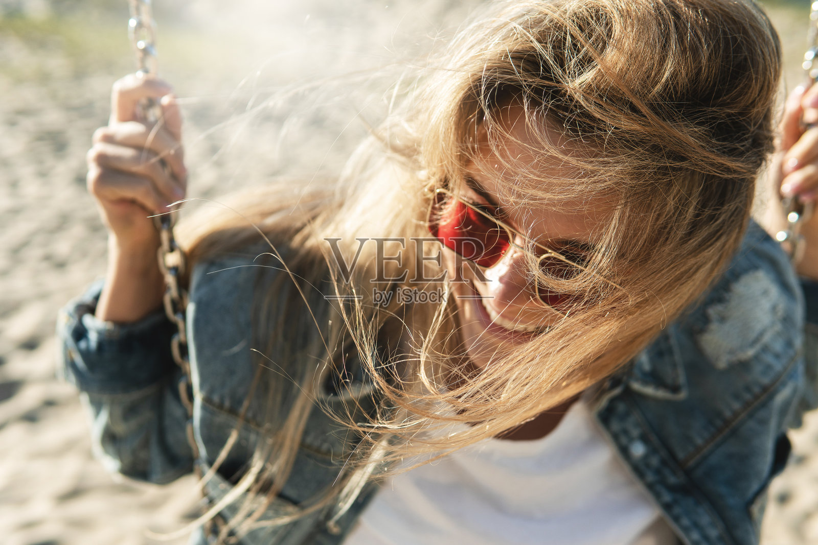 年轻微笑的女人坐在海滩的秋千上的特写镜头。照片摄影图片