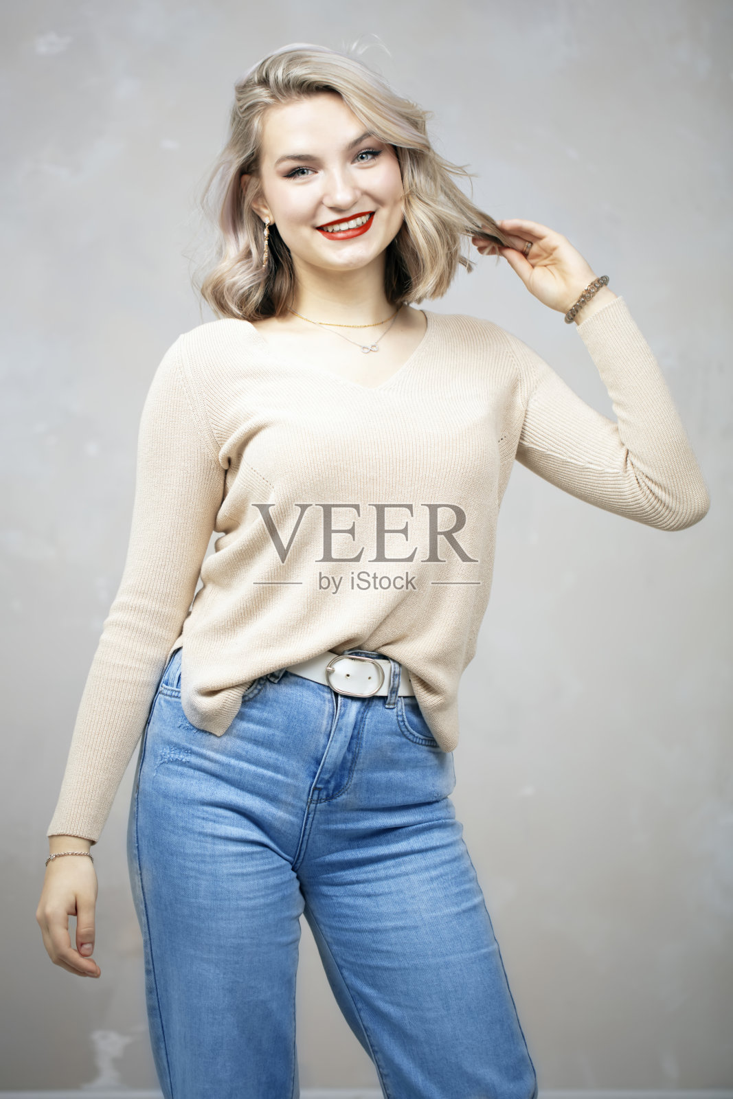 年轻漂亮的金发女孩，穿着牛仔裤和米色毛衣在镜头前摆姿势。照片摄影图片