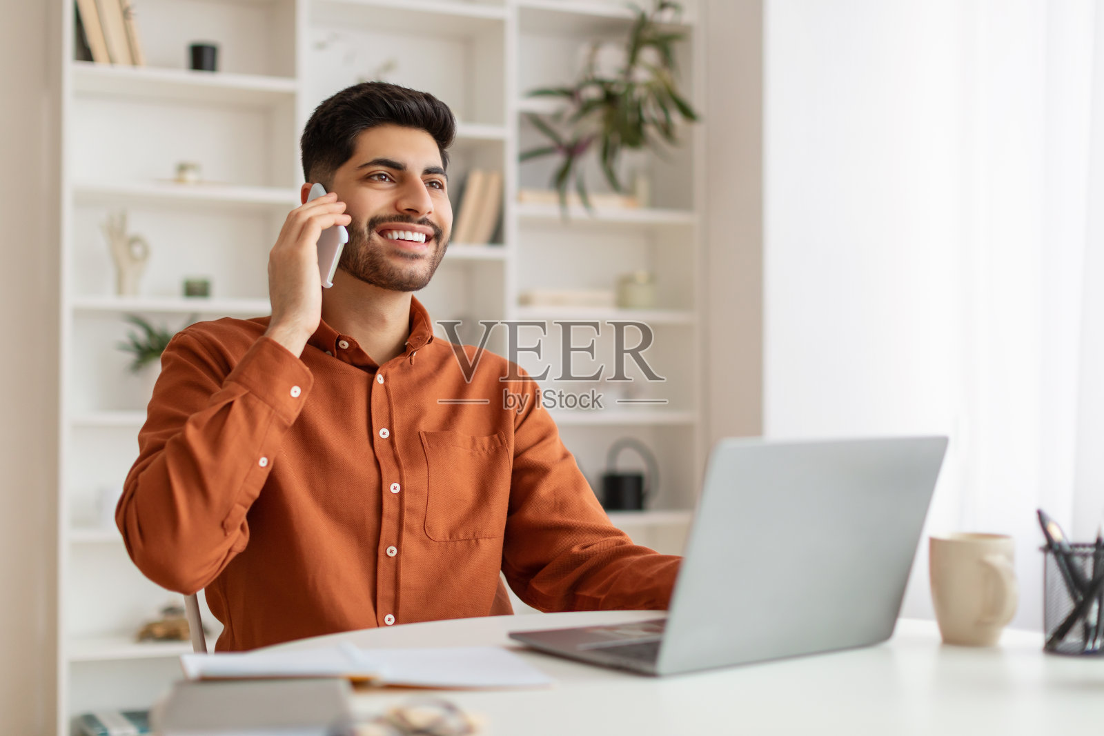 满脸笑容的大胡子男人一边工作一边在家里打电话照片摄影图片
