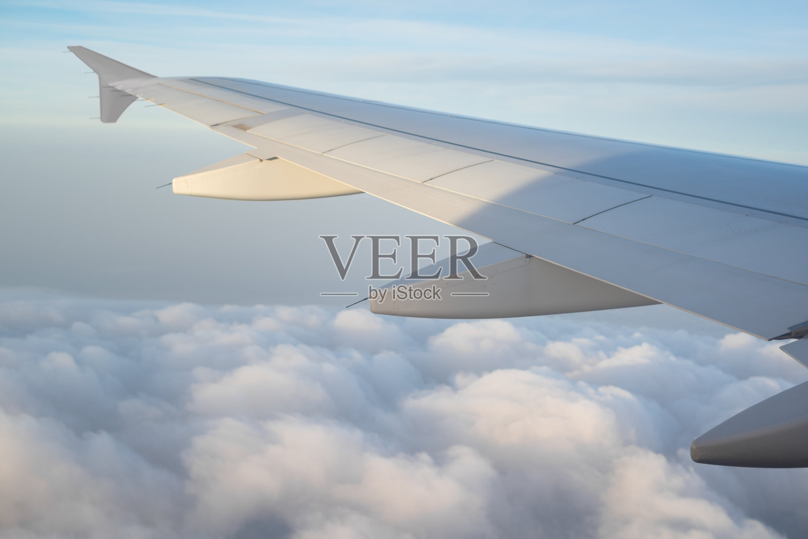 飞机的机翼在天空的云层上面飞行，从飞机的窗口观看。阳光从背后照射过来。飞机机翼视图背景从内部飞行和旅行的概念和广告。照片摄影图片