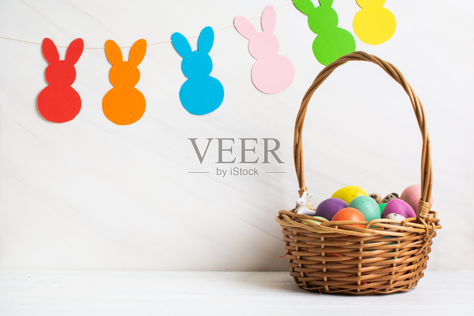 许多五彩缤纷的复活节彩蛋在柳条篮子与纸兔子花环照片摄影图片