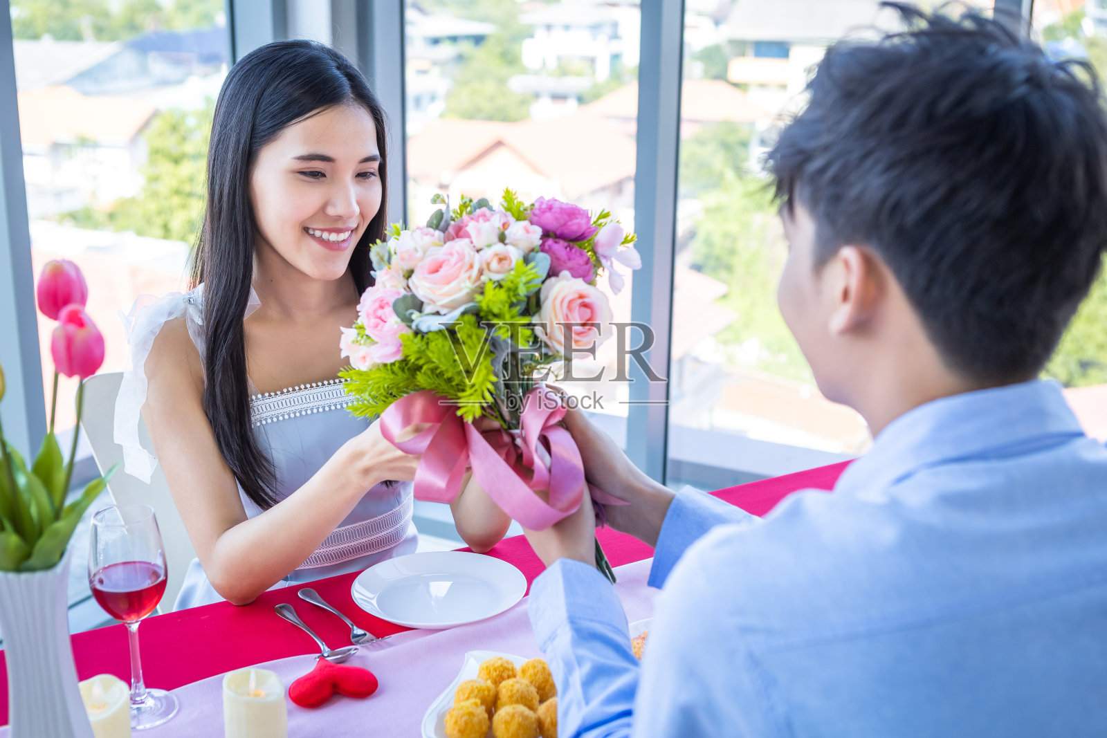 情人节和亚洲年轻幸福的情侣概念，一个男人拿着一束玫瑰给女人，双手在微笑，她的脸在午餐后等待惊喜在一家餐馆的背景照片摄影图片