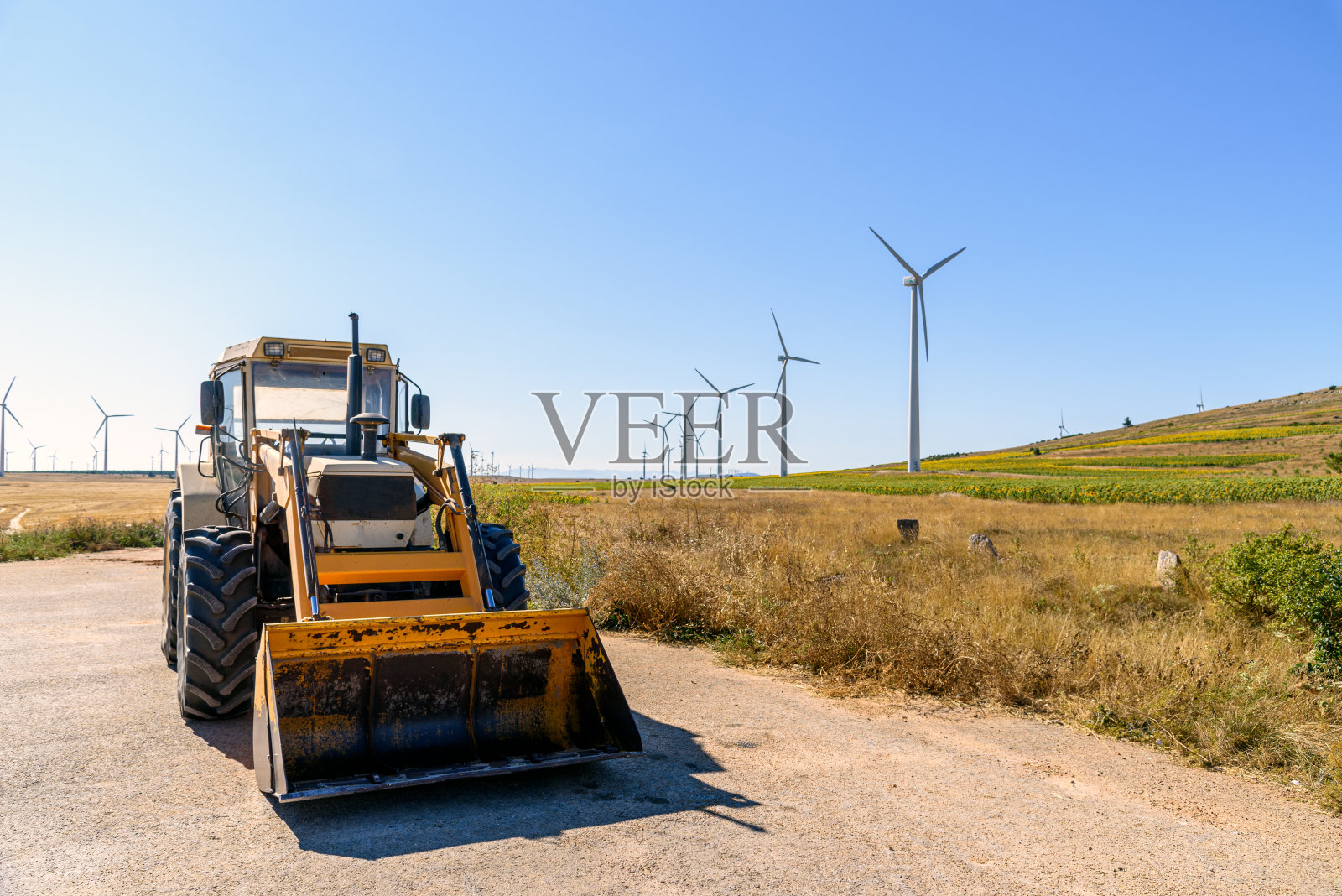 挖掘机对抗风力涡轮机发电的农田景观照片摄影图片