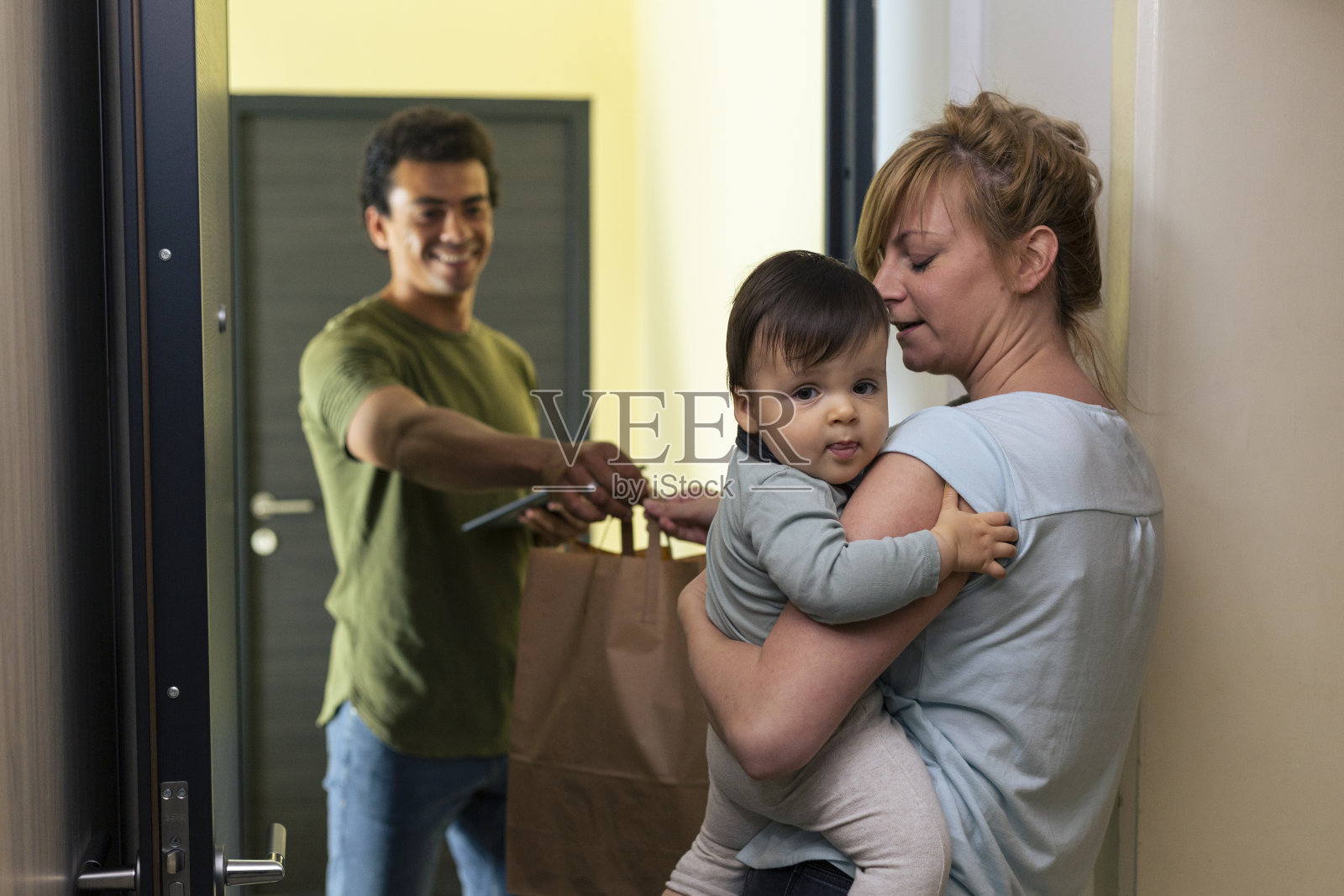 快递员给怀抱婴儿的母亲送包裹。照片摄影图片