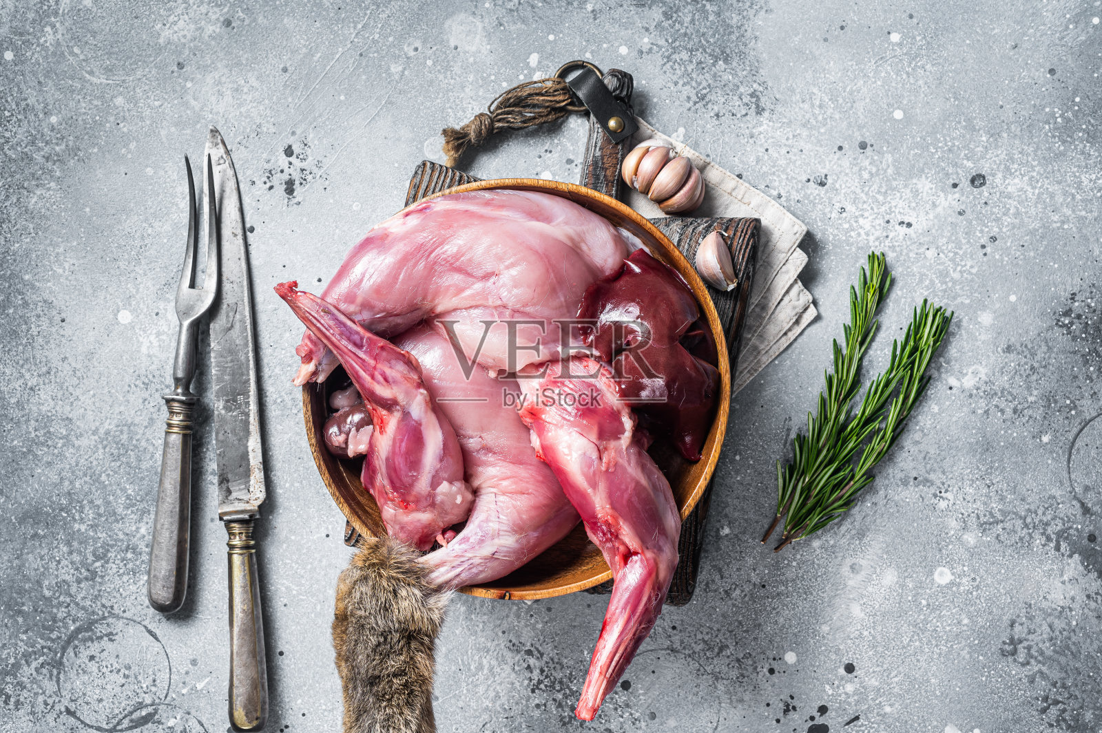 生野兔野味，腿和内脏在木盘与草药。灰色的背景。俯视图照片摄影图片