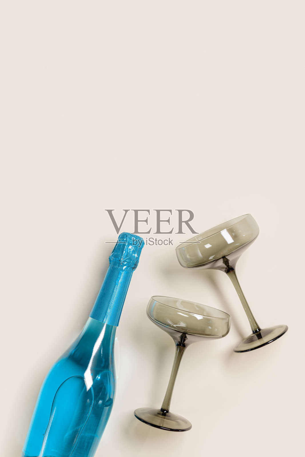 香槟酒杯，灰色玻璃，蓝色香槟或蓝色气泡酒瓶。灯光节日饮品概念，炫目阳光。现代葡萄酒色玻璃杯。创意平面躺照片摄影图片