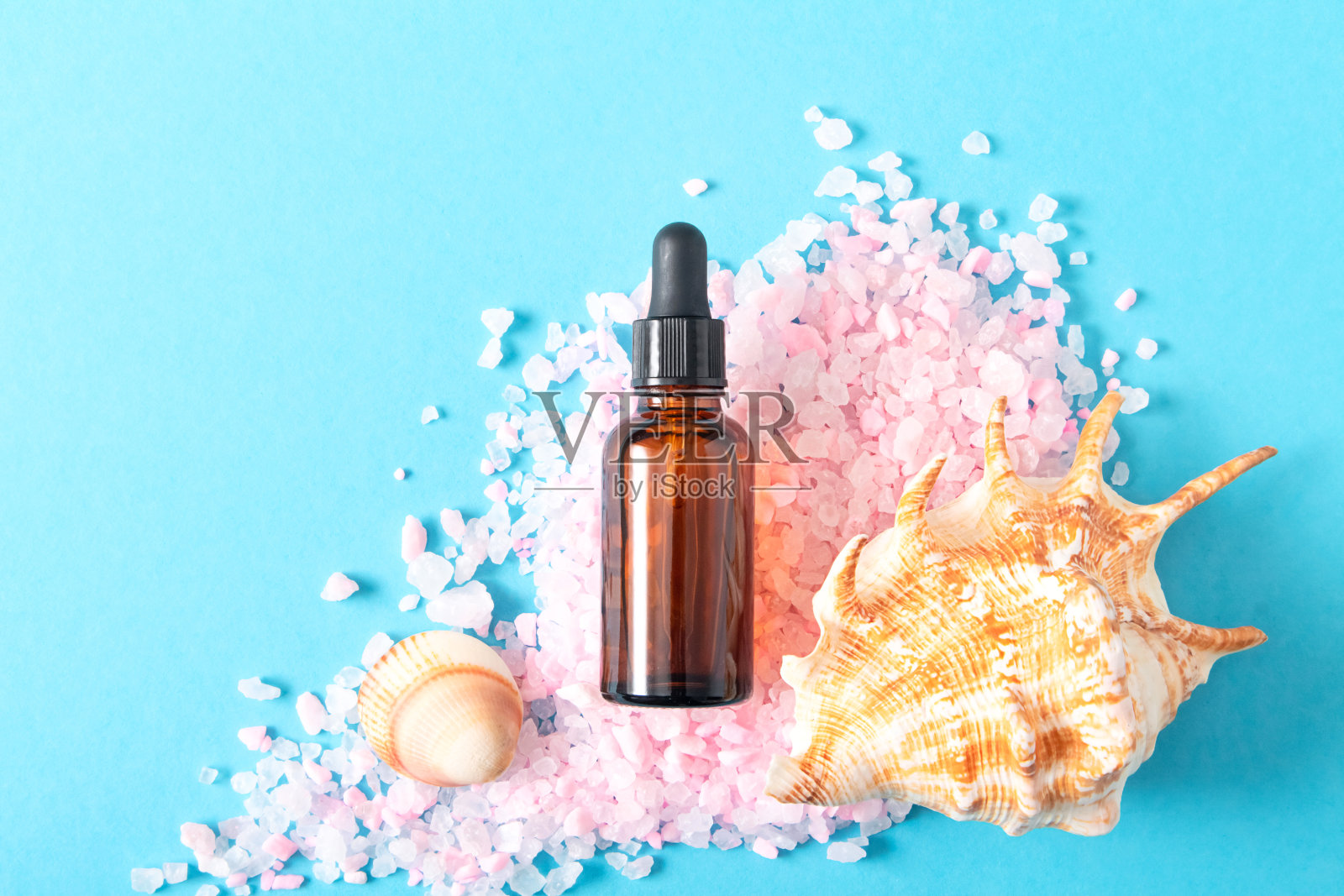 滴黑色玻璃化妆品瓶模拟，粉红色的海盐和贝壳在蓝色的背景。环保护理有机产品。美容、水疗理念。副本的空间。照片摄影图片