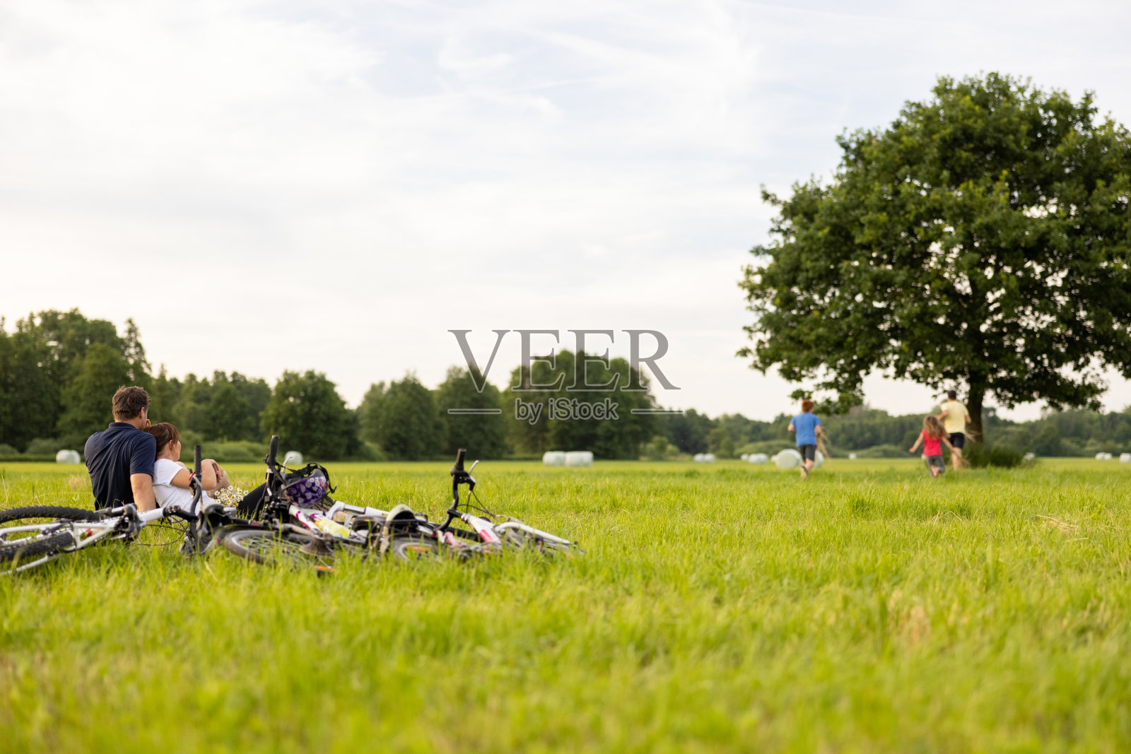 父母们骑自行车旅行结束后，坐在草地上休息，孩子们在大自然的树下玩耍照片摄影图片