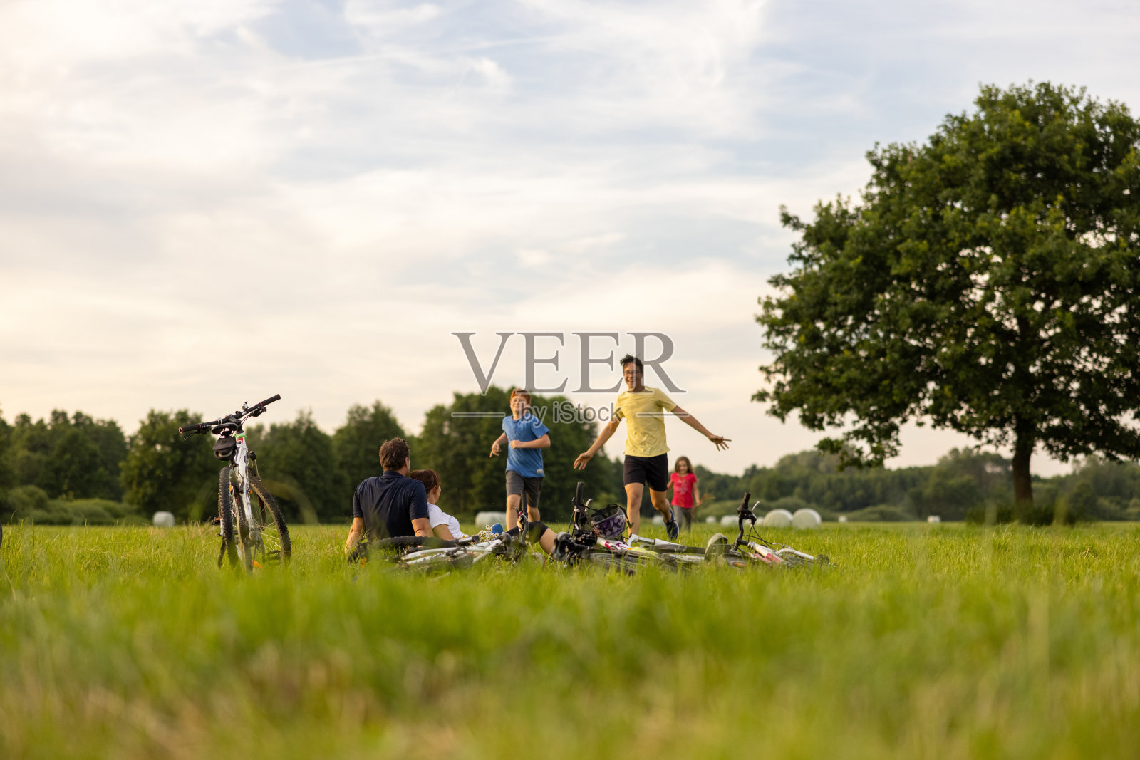 孩子们顽皮地跑向坐在草地上休息的父母，自行车在最前面照片摄影图片