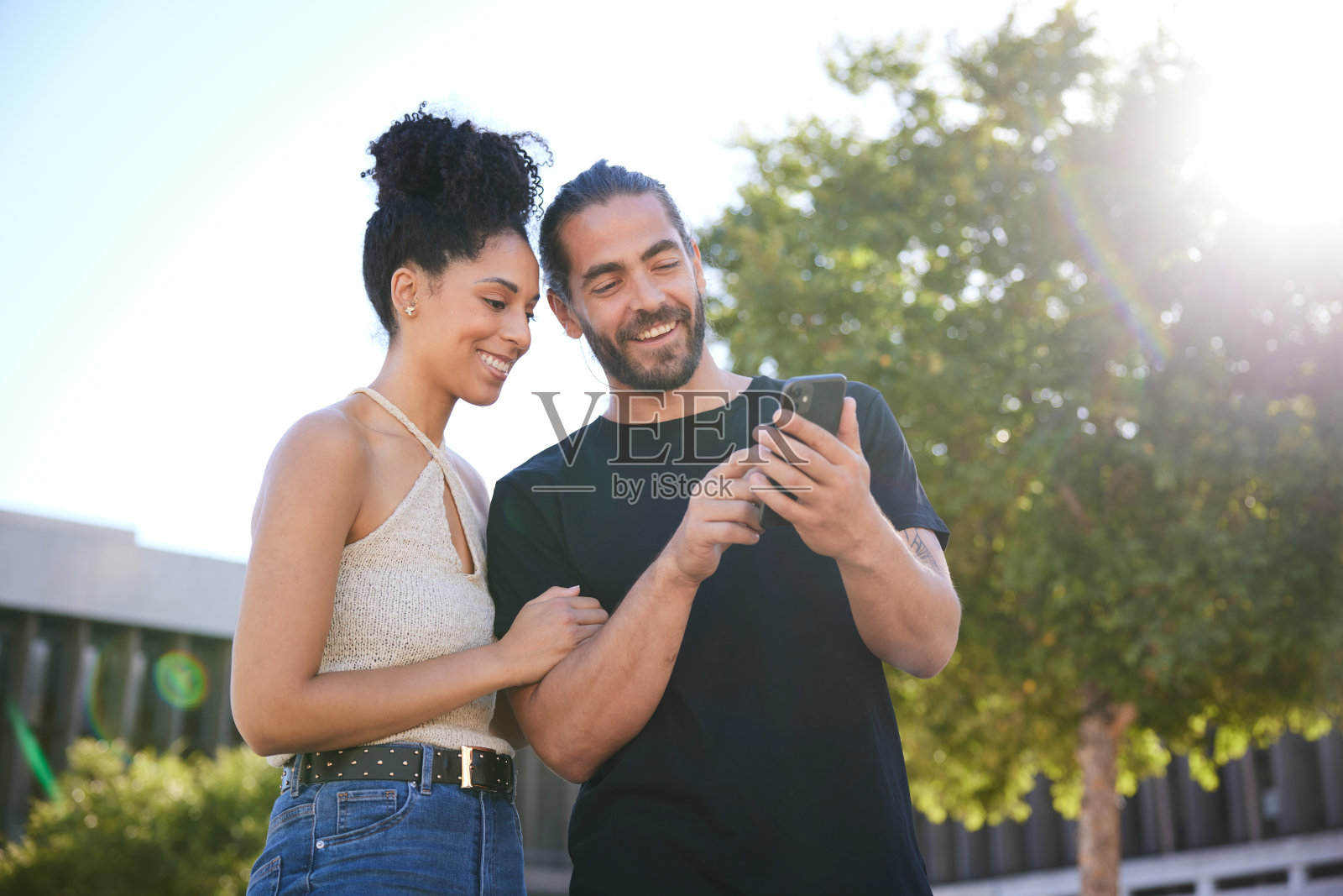 一对微笑的年轻夫妇一边走在城里一边看手机照片摄影图片