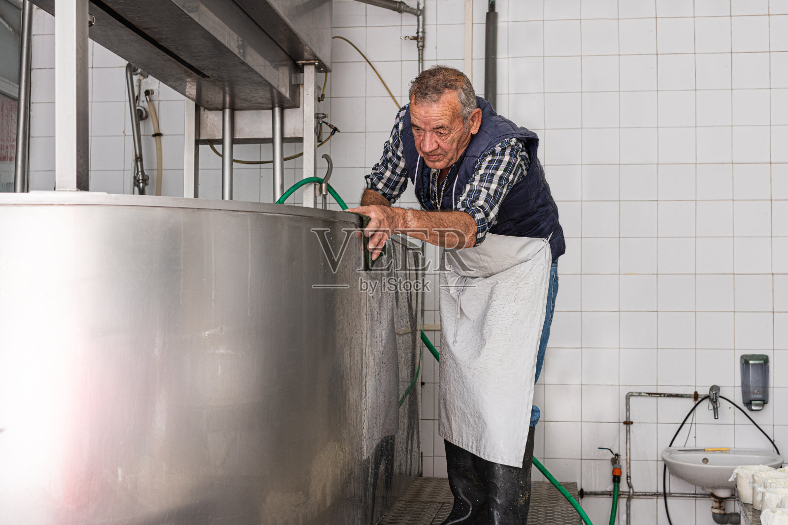 一个穿着围裙的老人在擦洗不锈钢容器的外面照片摄影图片